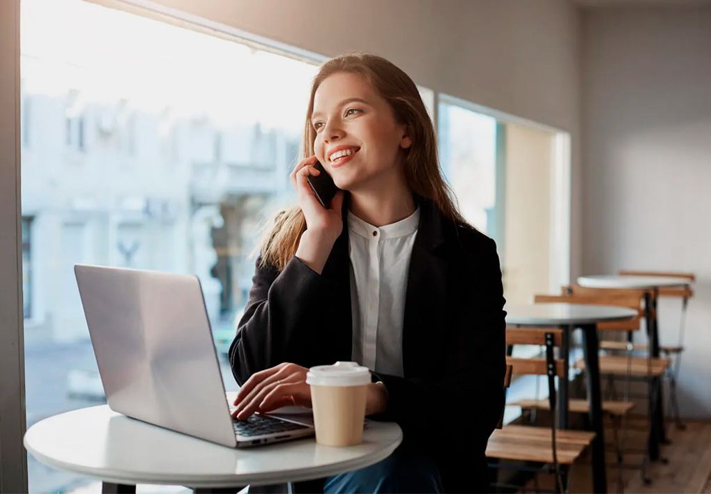 Chica hablando por el móvil y consultando un ordenador para transferir su dominio a Arsys