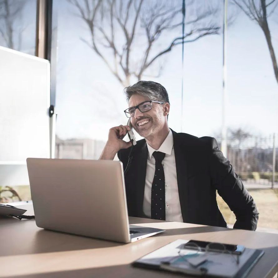 Señor habla por teléfono y consulta su portátil satisfecho porque garantizamos el máximo rendimiento y disponibilidad para su proyecto