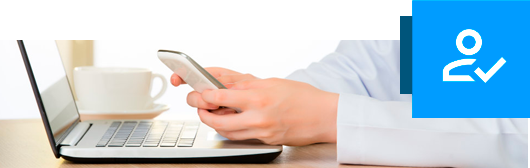 Manos teclean en un móvil frente a un portátil