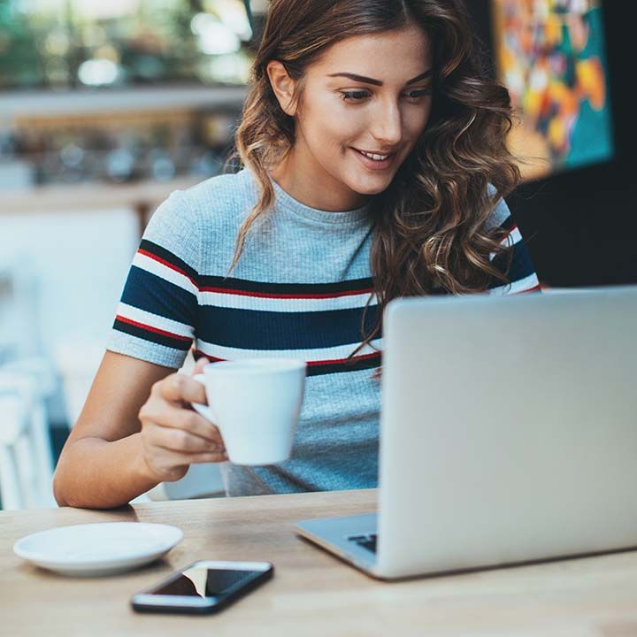 Chica toma café mientras consulta su Webmail de Arsys en un portátil