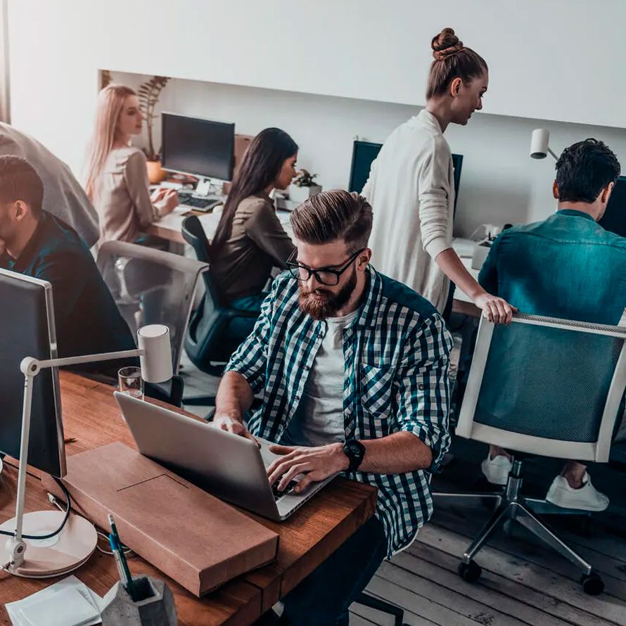 En una oficina, rodeado de muchos compañeros, un chico teclea en su ordenador para consultar el Whois / RDAP de Dominios